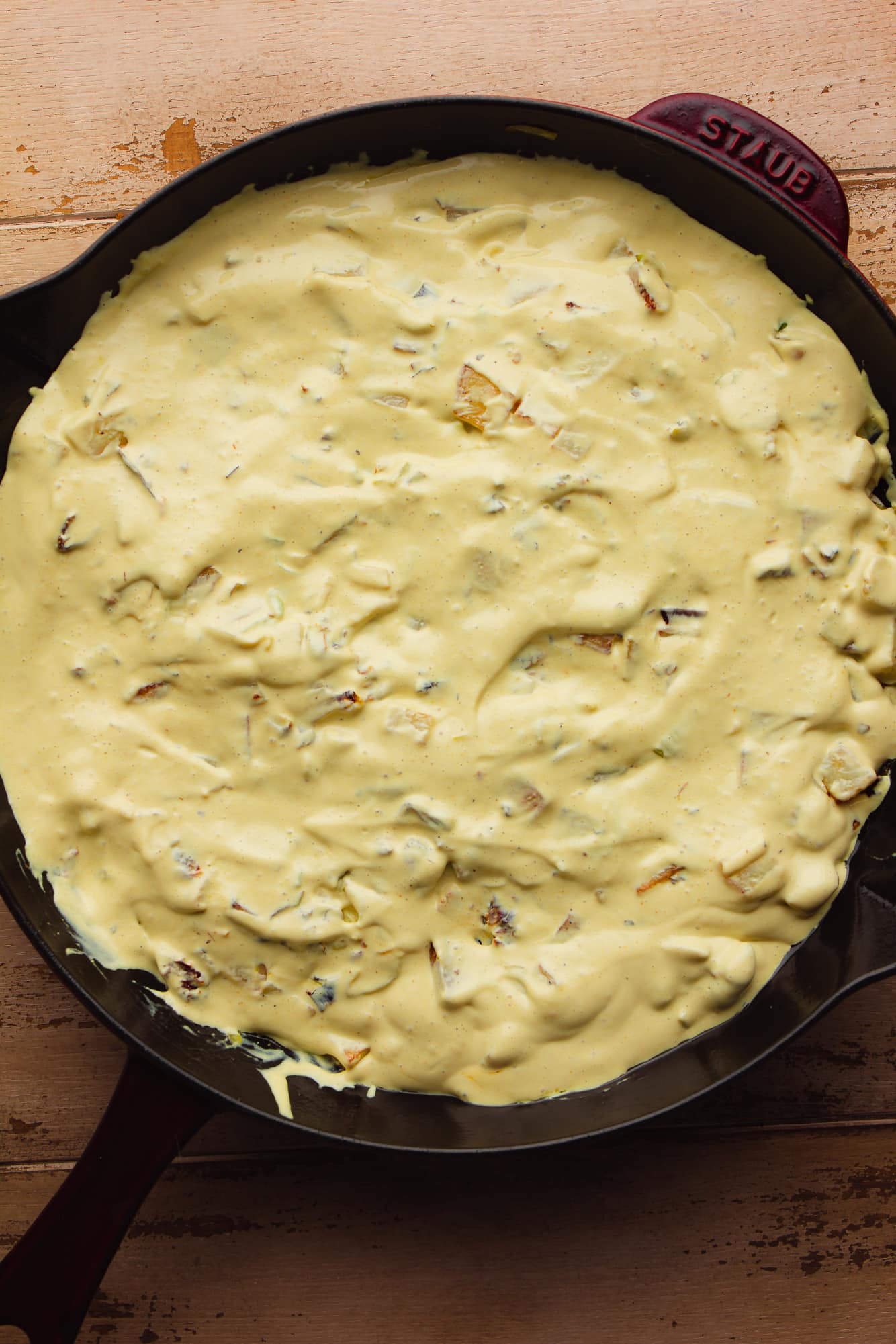 cooked vegetables topped with a creamy yellow sauce in a large black skillet.