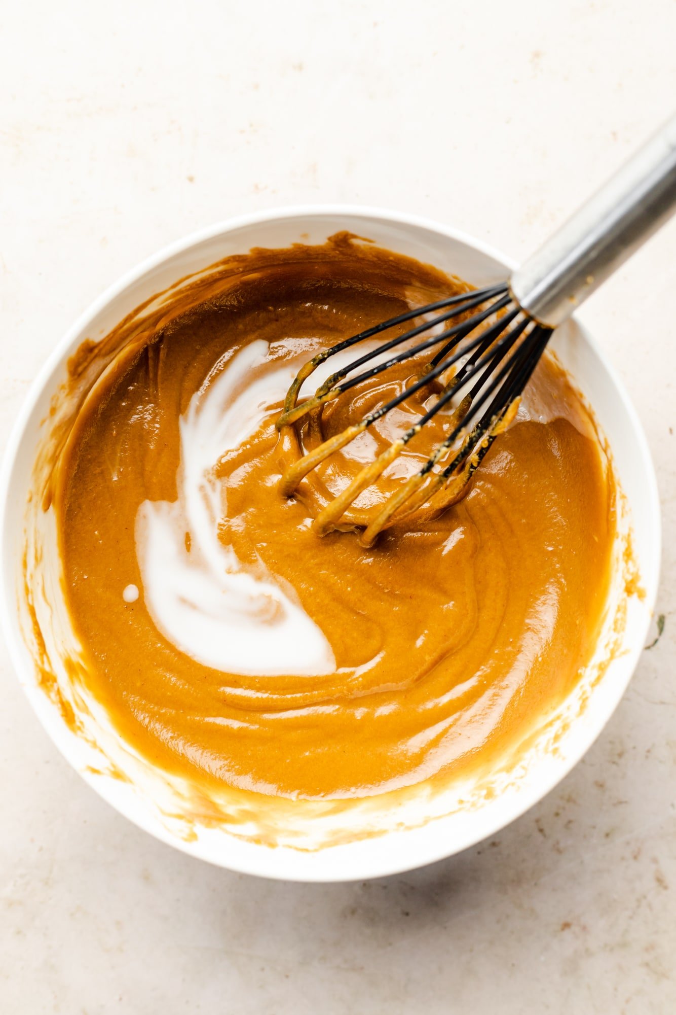 using a whisk to stir coconut milk into a bowl of peanut sauce.