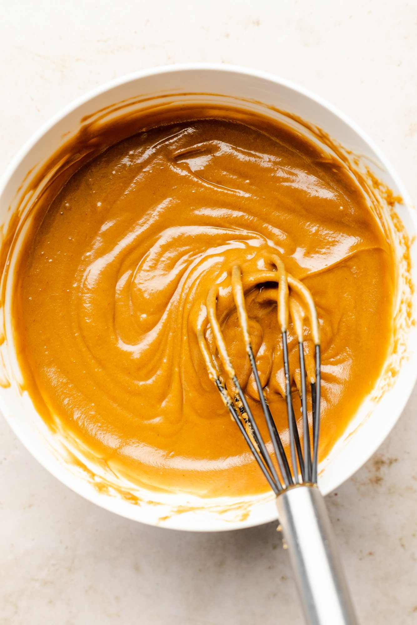 whisking peanut sauce in a white bowl.