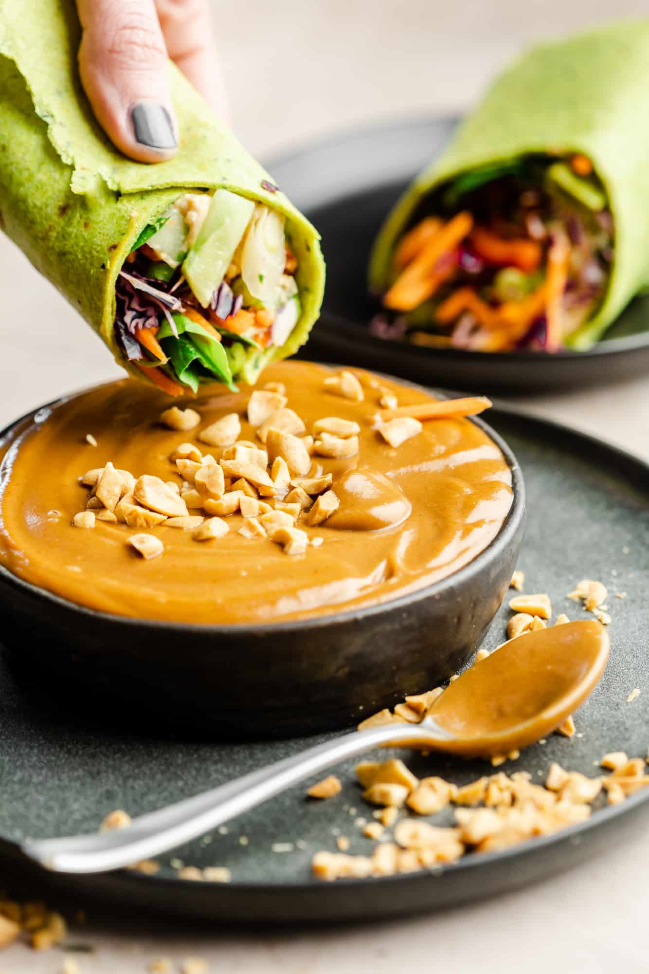Dipping vegetable wraps in a bowl of peanut sauce.