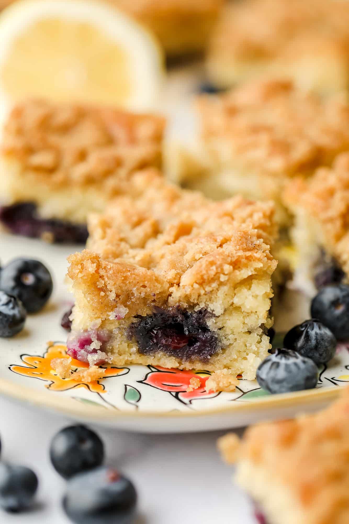 close up on a slice of blueberry coffee cake on a plate surrounded by fresh blueberries.