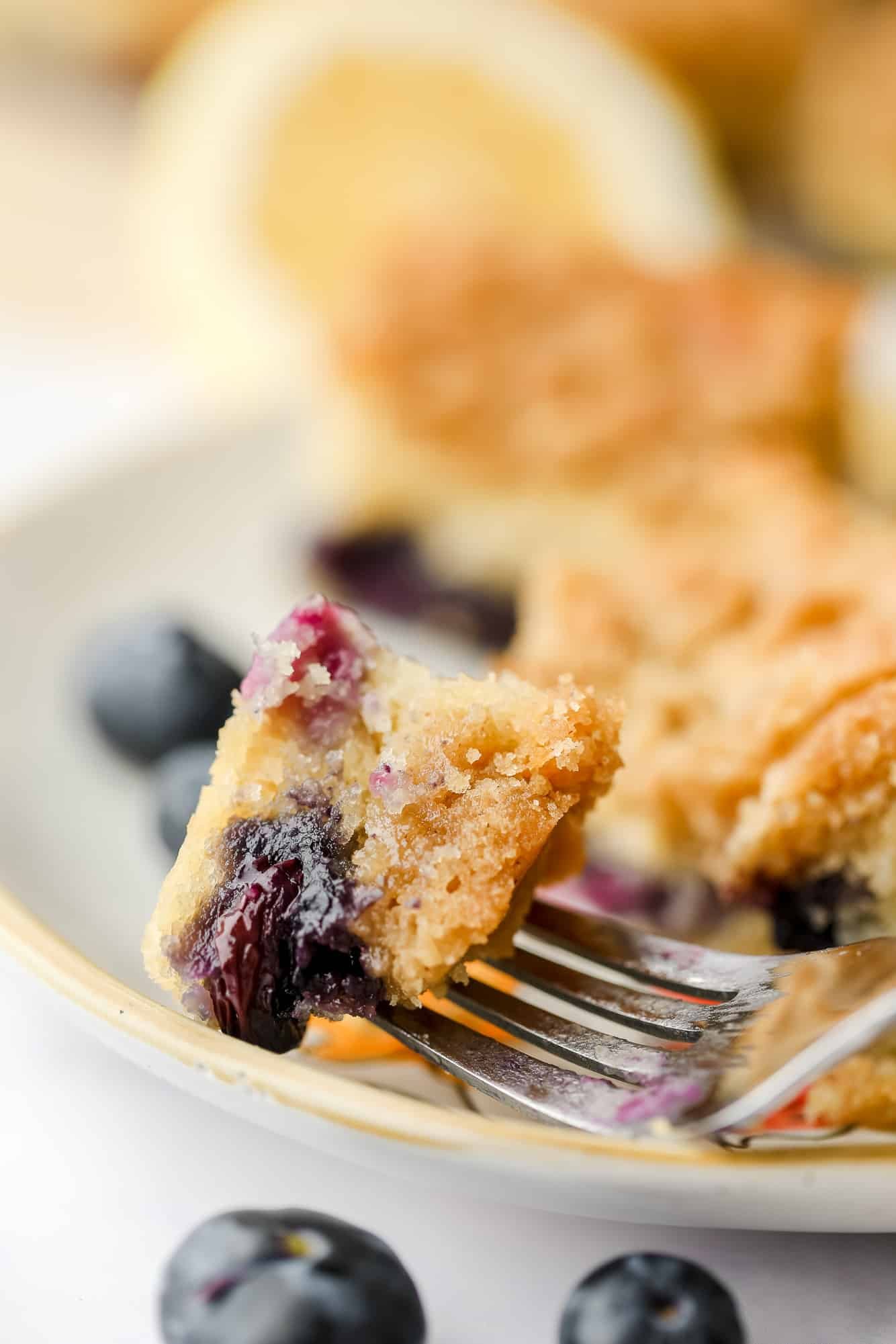 close up on a fork holding a bite of blueberry coffee cake on a plate.