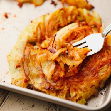 a metal fork scooping up a piece of roasted cabbage from a cabbage steak.