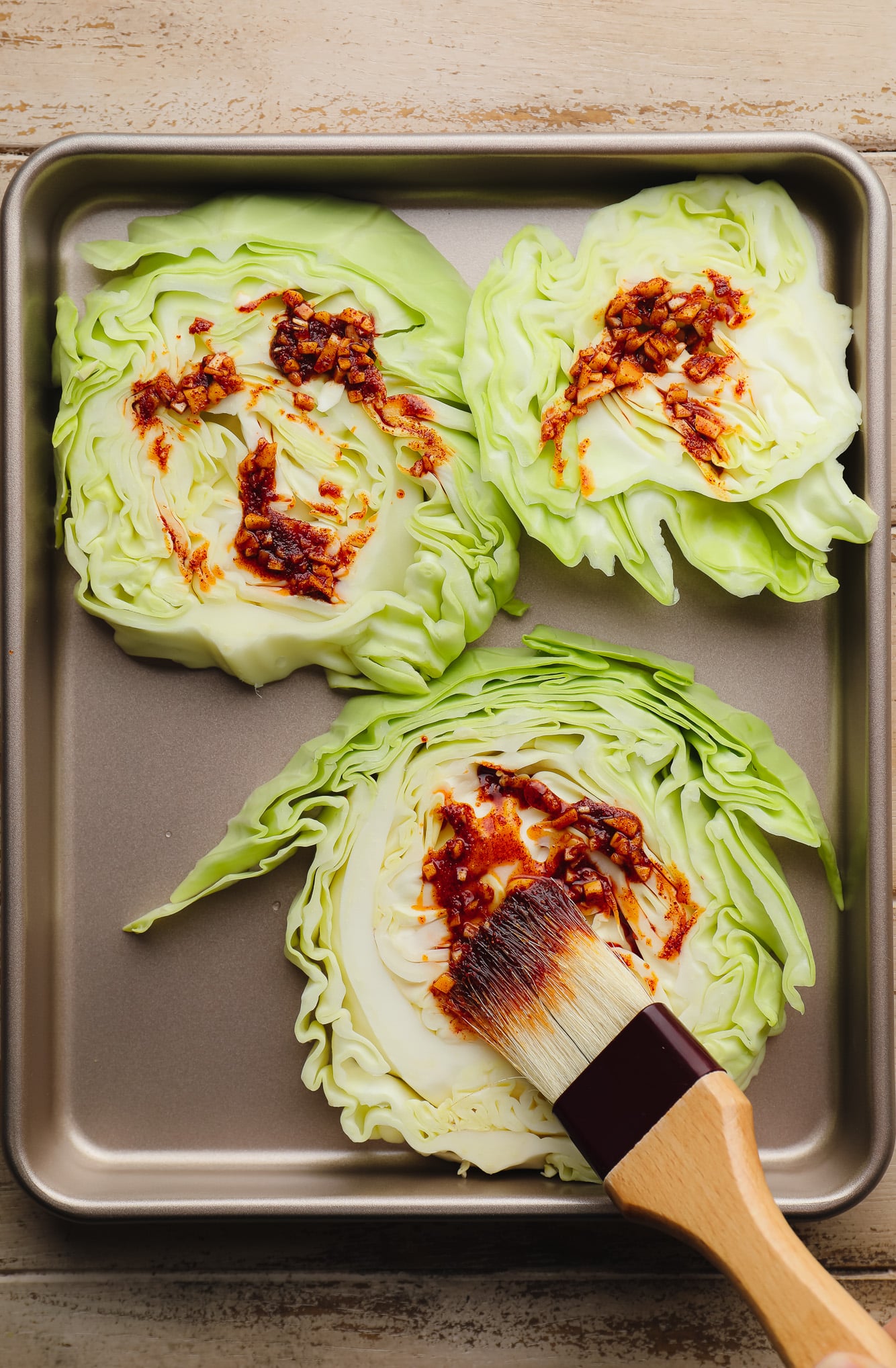 using a pastry brush to brush a seasoning mixture onto sliced cabbage steaks.