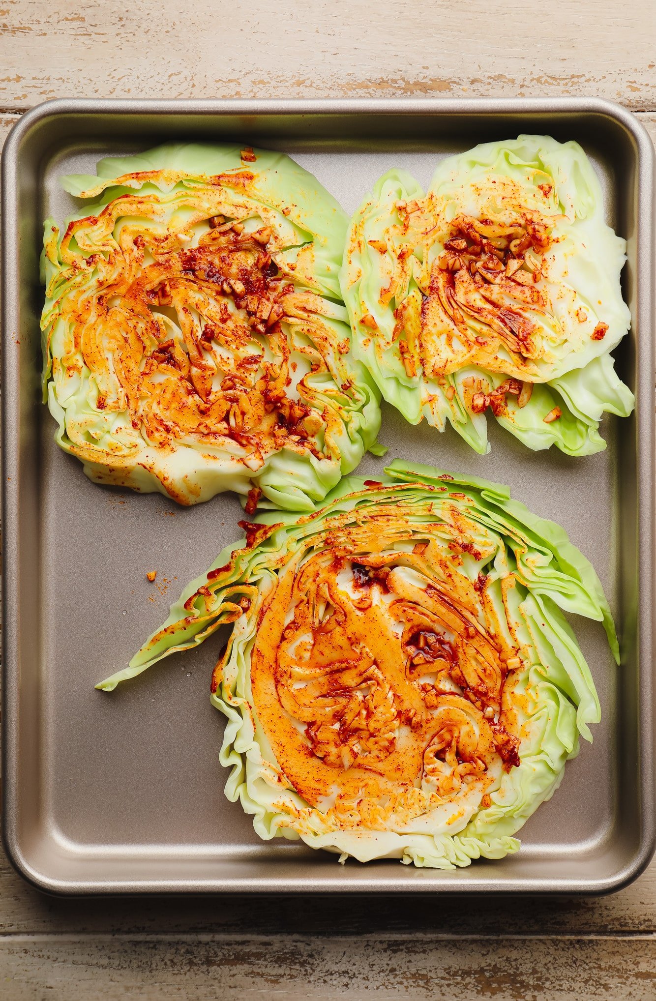 cabbage steaks brushed with oil and seasonings on a metal baking sheet.