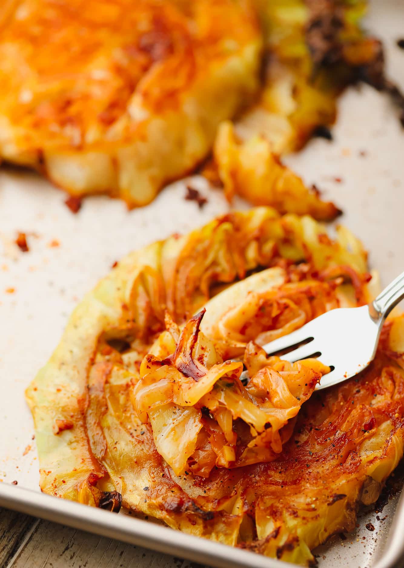 a metal fork scooping up a piece of roasted cabbage from a cabbage steak.