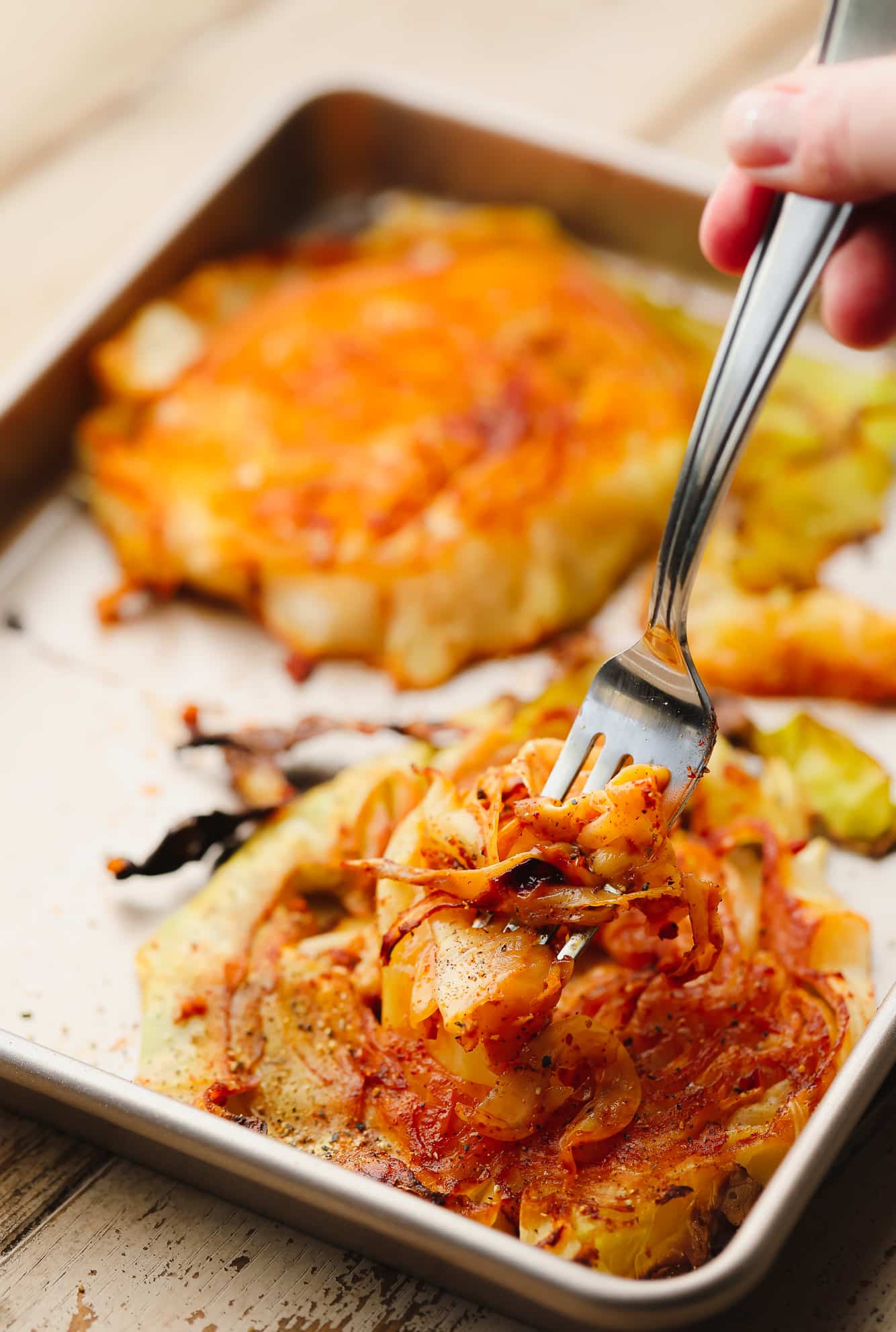 a metal fork scooping up a piece of roasted cabbage from a cabbage steak.