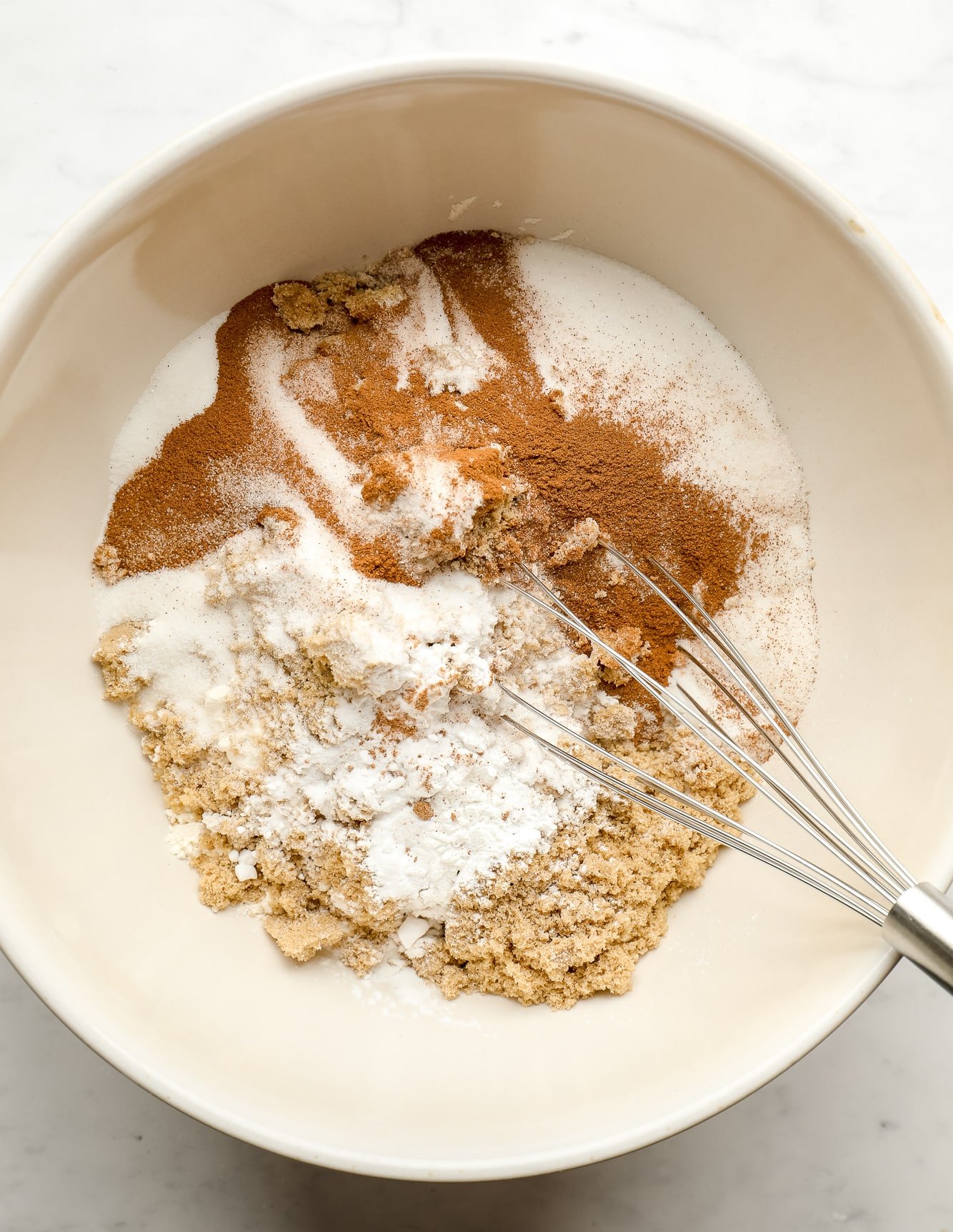 whisking flour, sugar, and spices together in a large white bowl.