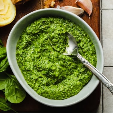 a grey bowl filled with spinach pesto with a metal spoon on top.