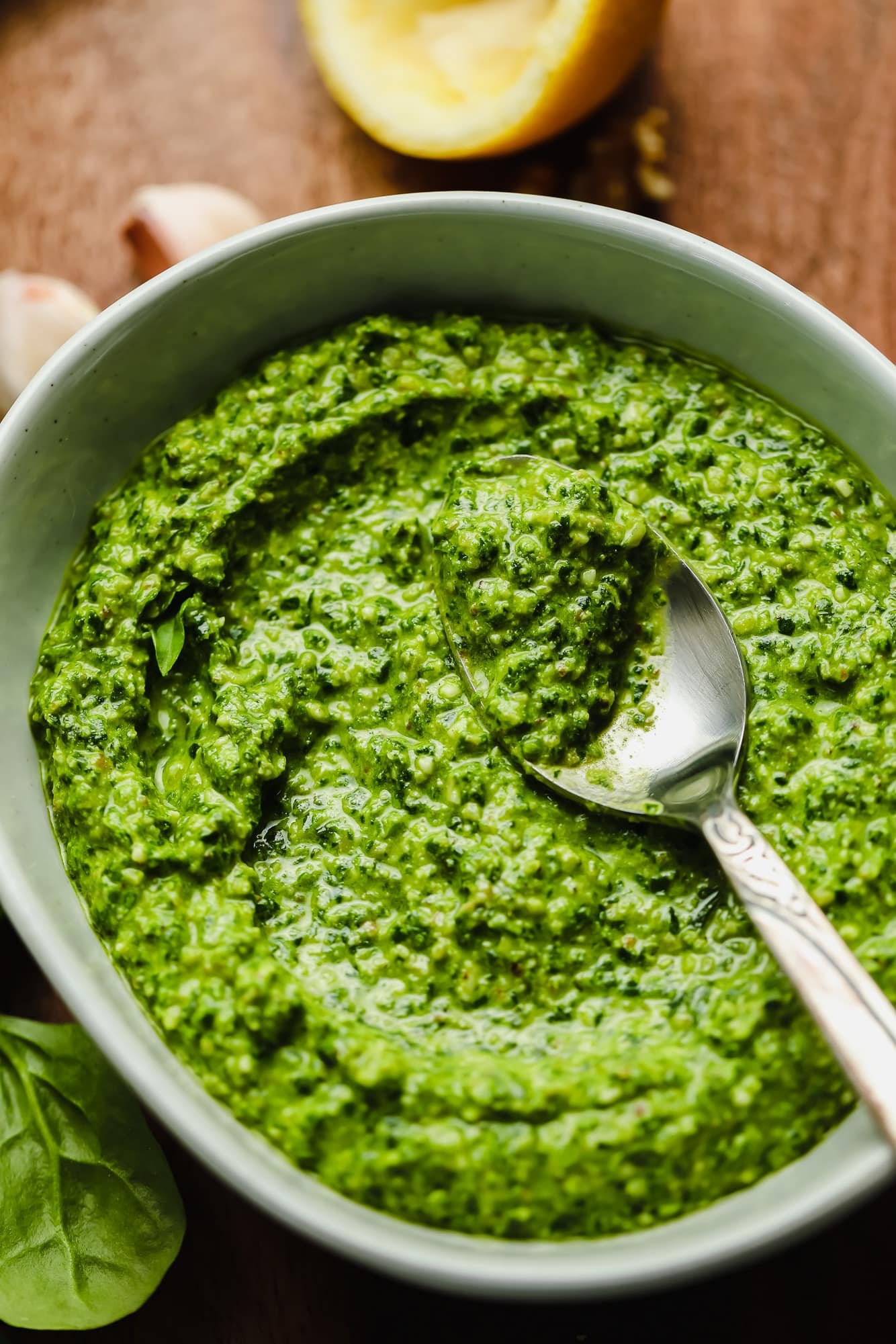 a grey bowl filled with spinach pesto with a metal spoon on top.