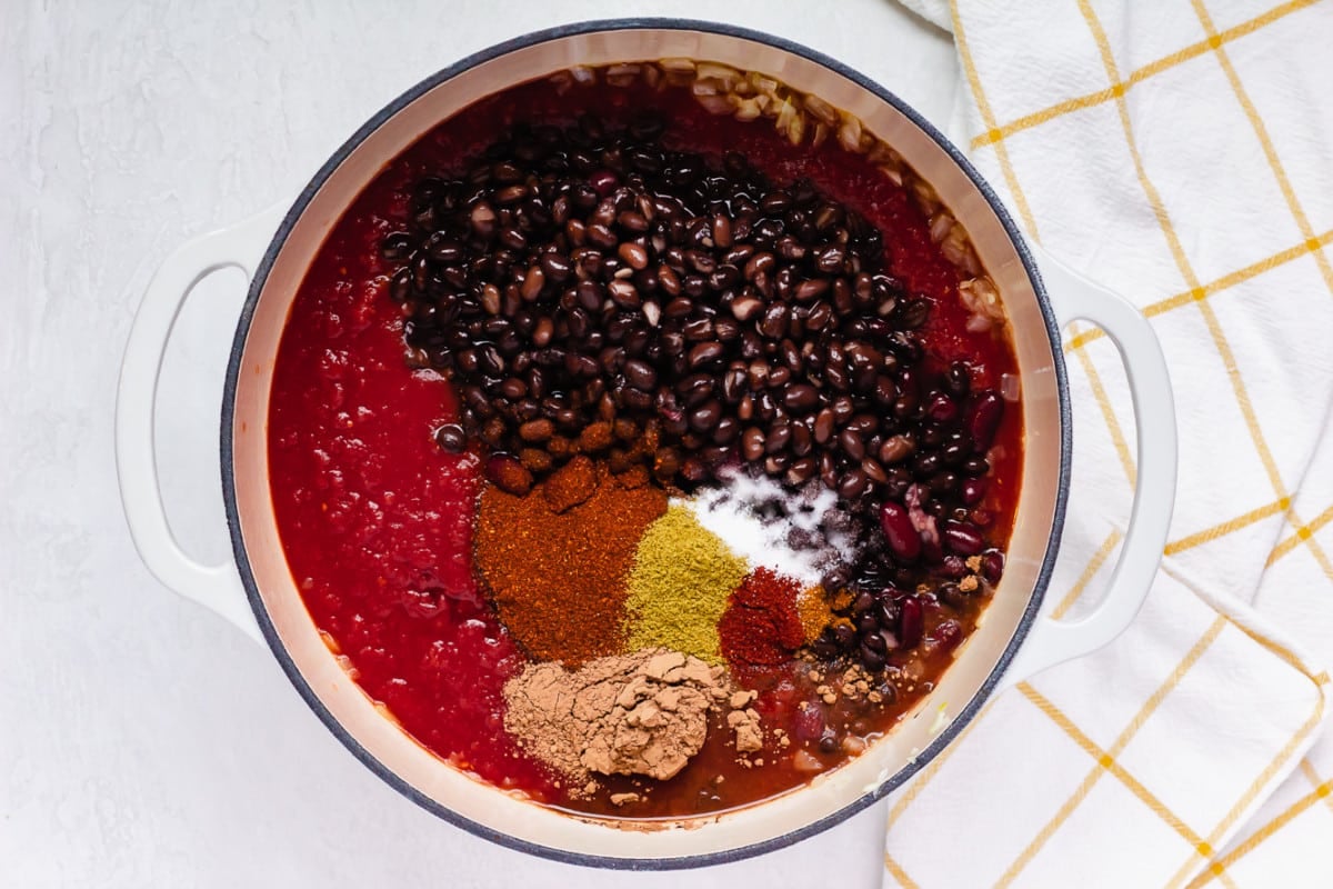 black beans, tomato sauce and spices in a white pot, not yet stirred together.