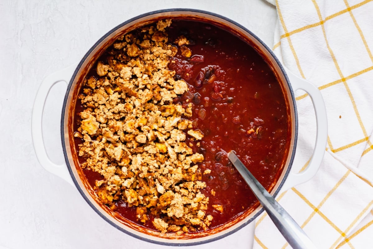 adding cooked crumbed tofu to the pot with the chili