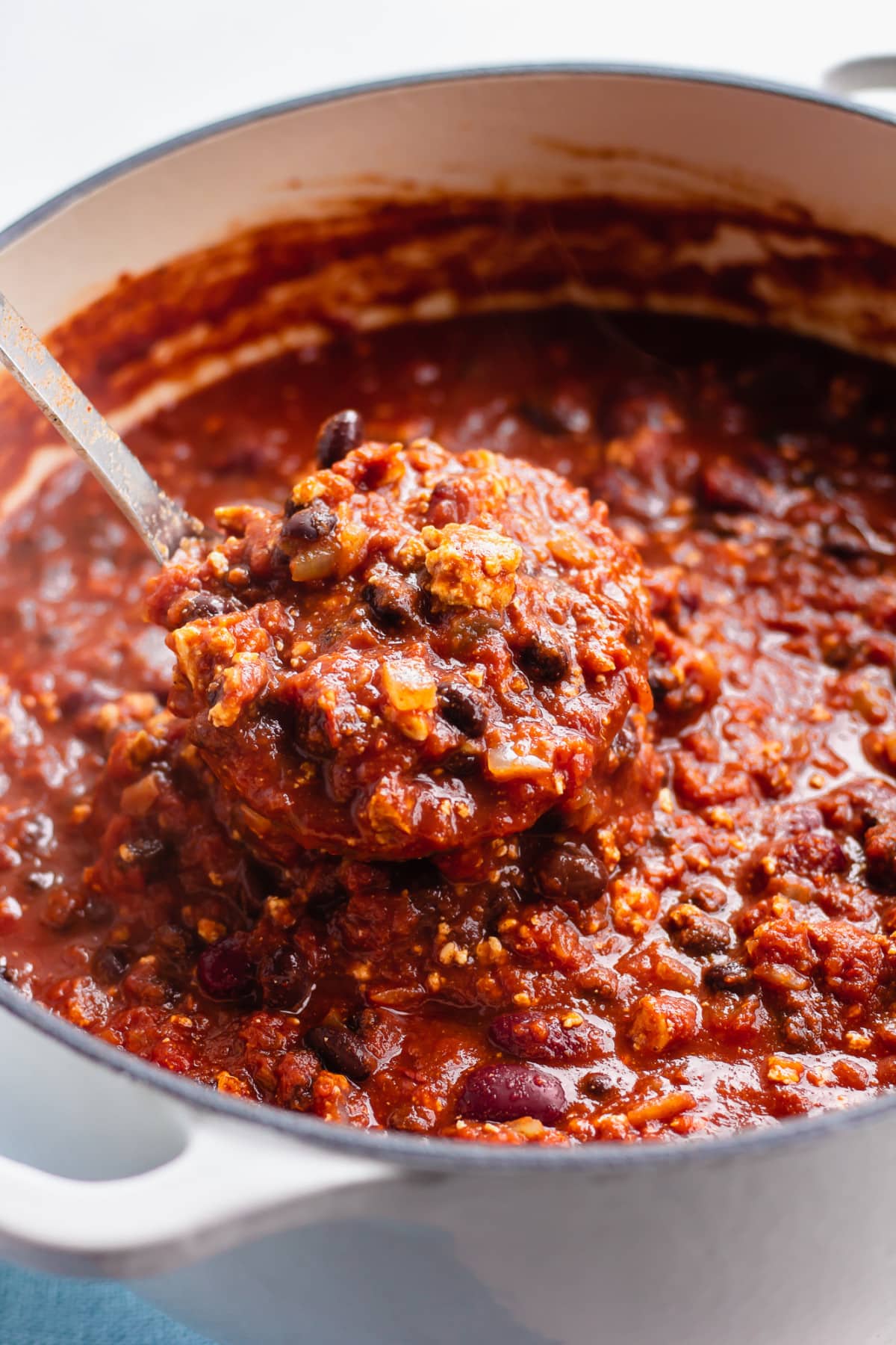 white pot full of vegan chili, a ladle scooping out a serving.