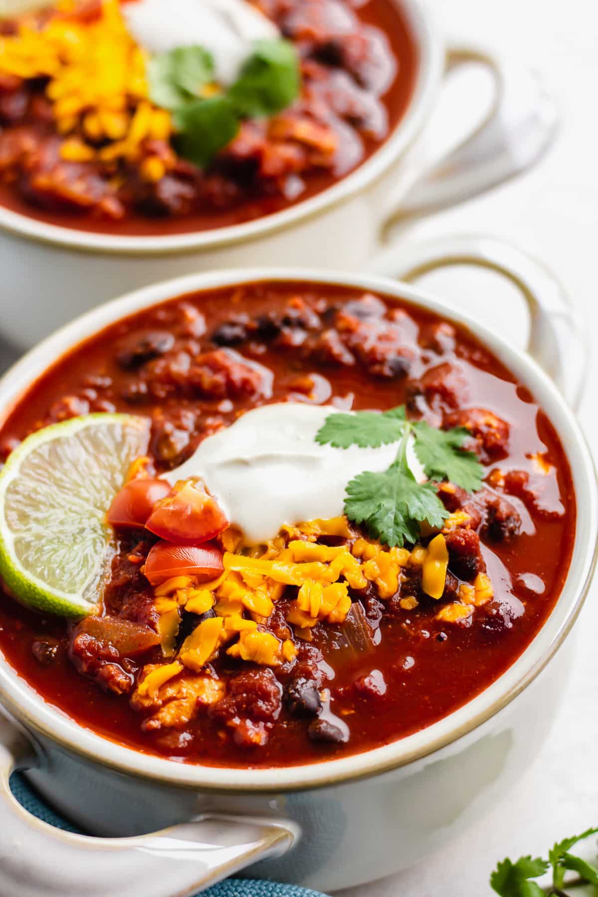 close up of a bowl with bean chili, sour cream, cheese and a lime wedge.