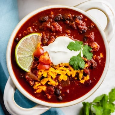 square image of a bowl of chili with handles, blue towel in background.