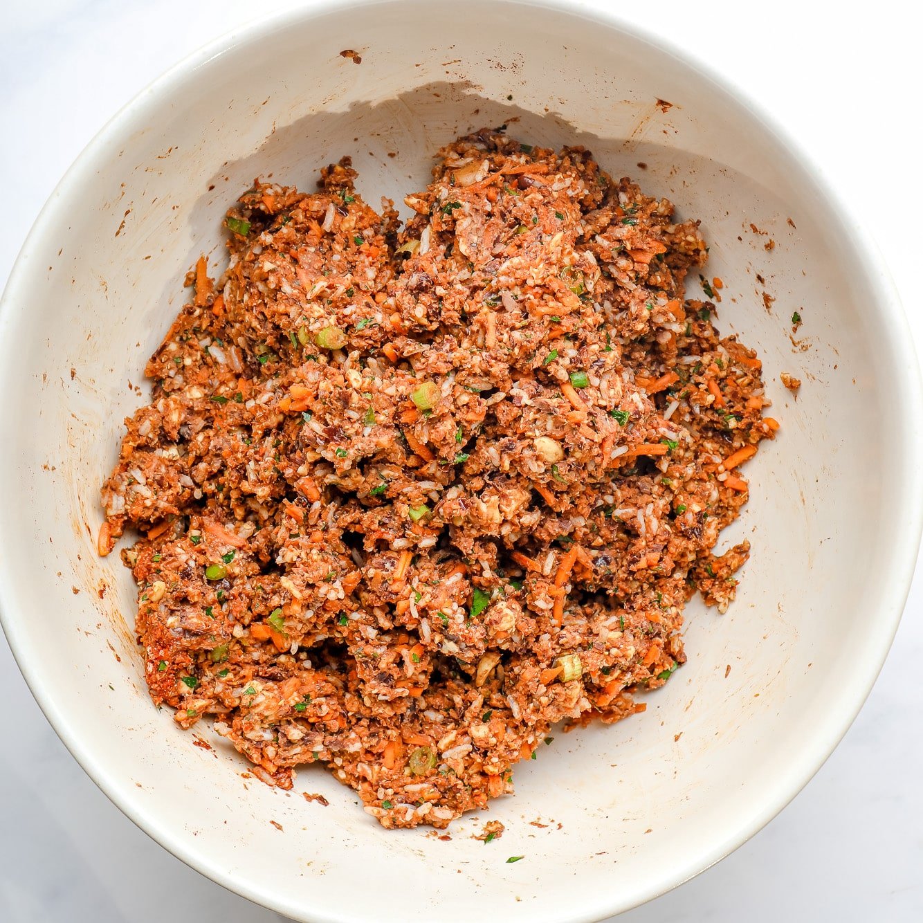 the ingredients for veggie burgers mixed together in a large white bowl.