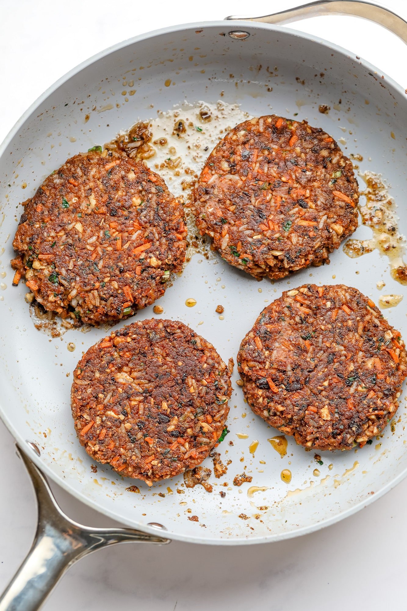 4 veggie burgers cooking in a large skillet.