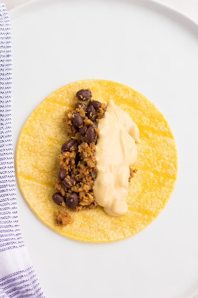 small corn tortilla with bean filling, cheese sauce on white plate