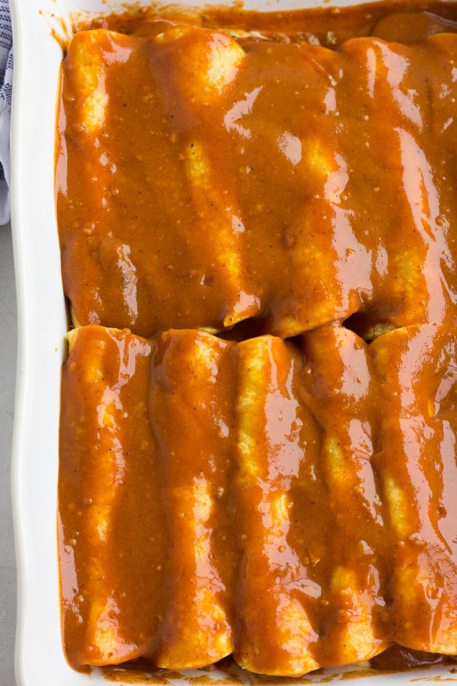 red sauce over rolled tortillas in a big white dish