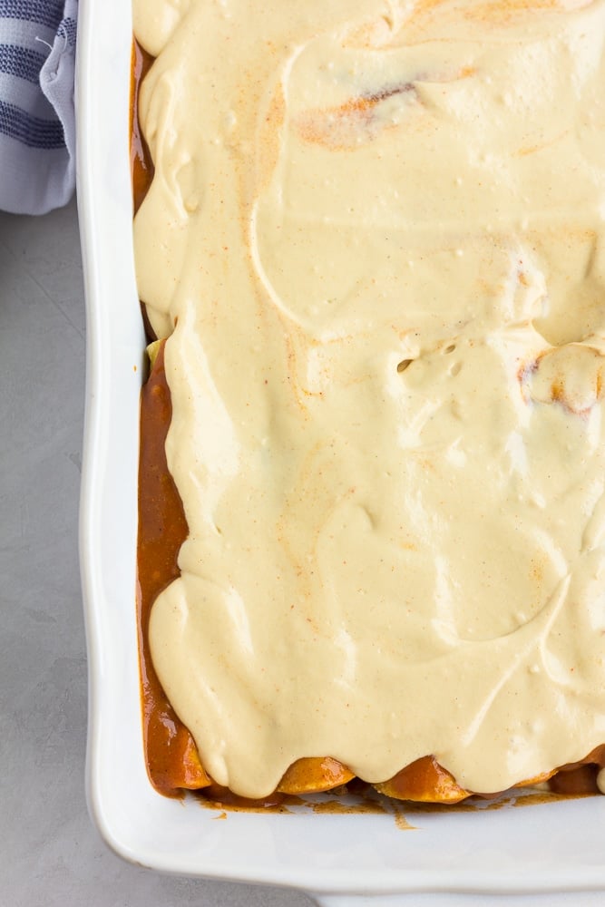creamy white sauce covering red enchiladas in a casserole dish