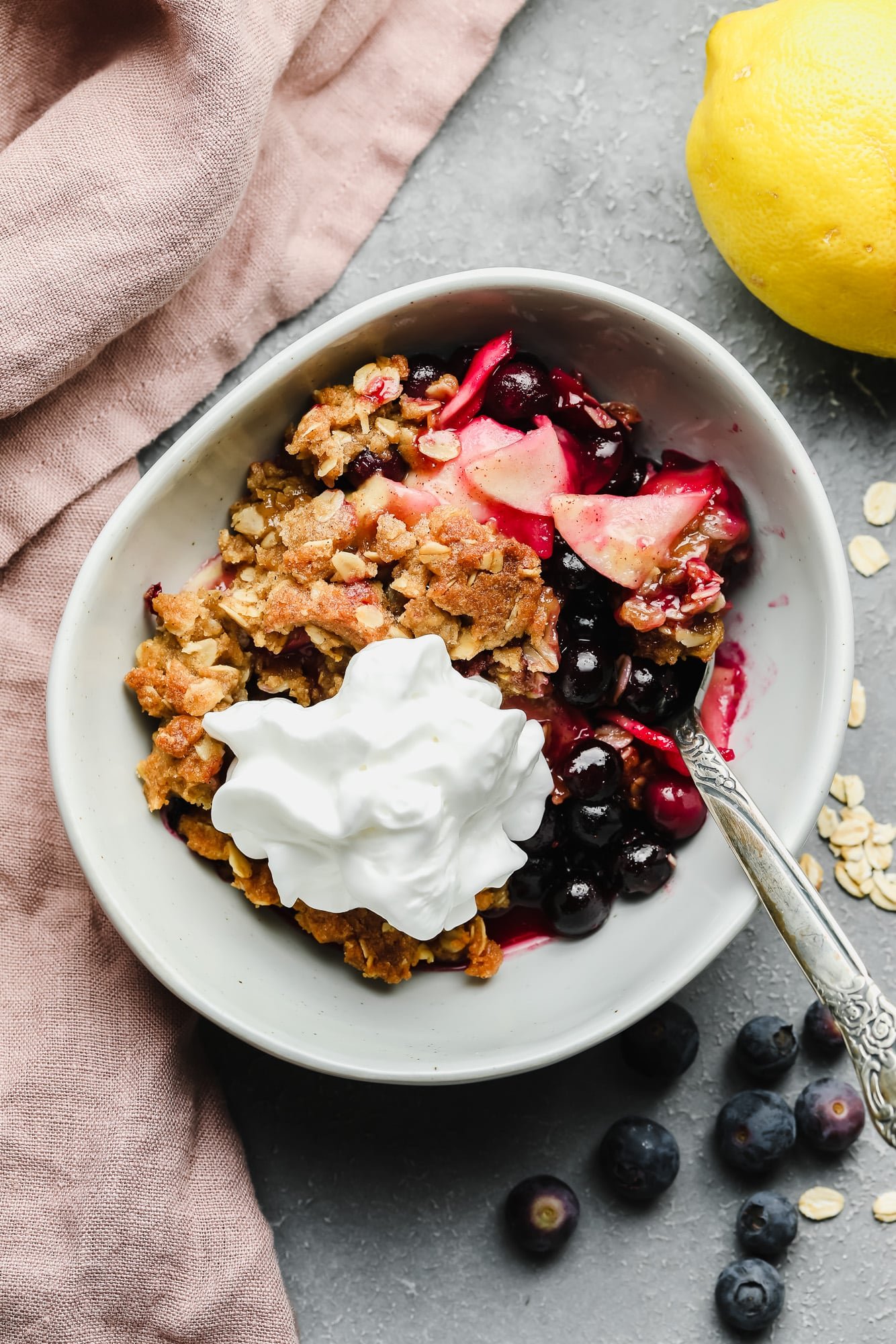 a serving of apple and blueberry crumble in a white bowl with vegan whipped cream on top.