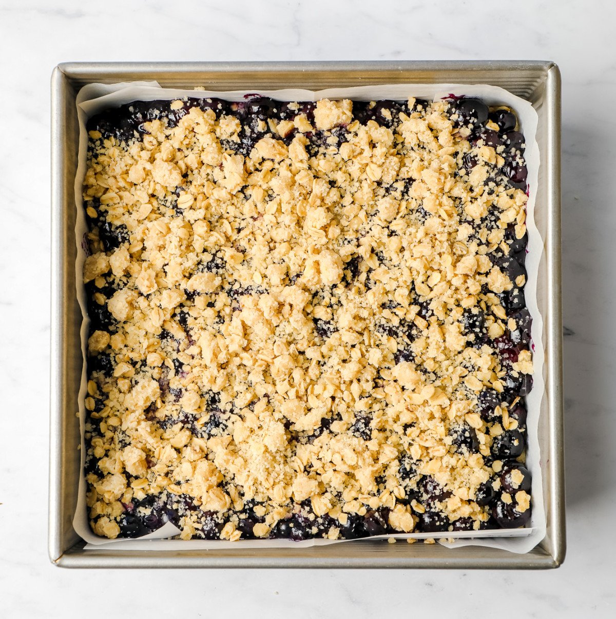 uncooked crumb mixture with berries underneath in a square pan