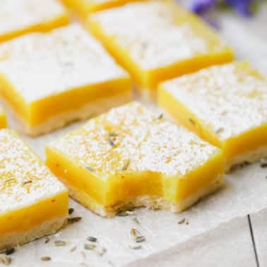 square image of several lemon bars with lavender flakes on parchment paper
