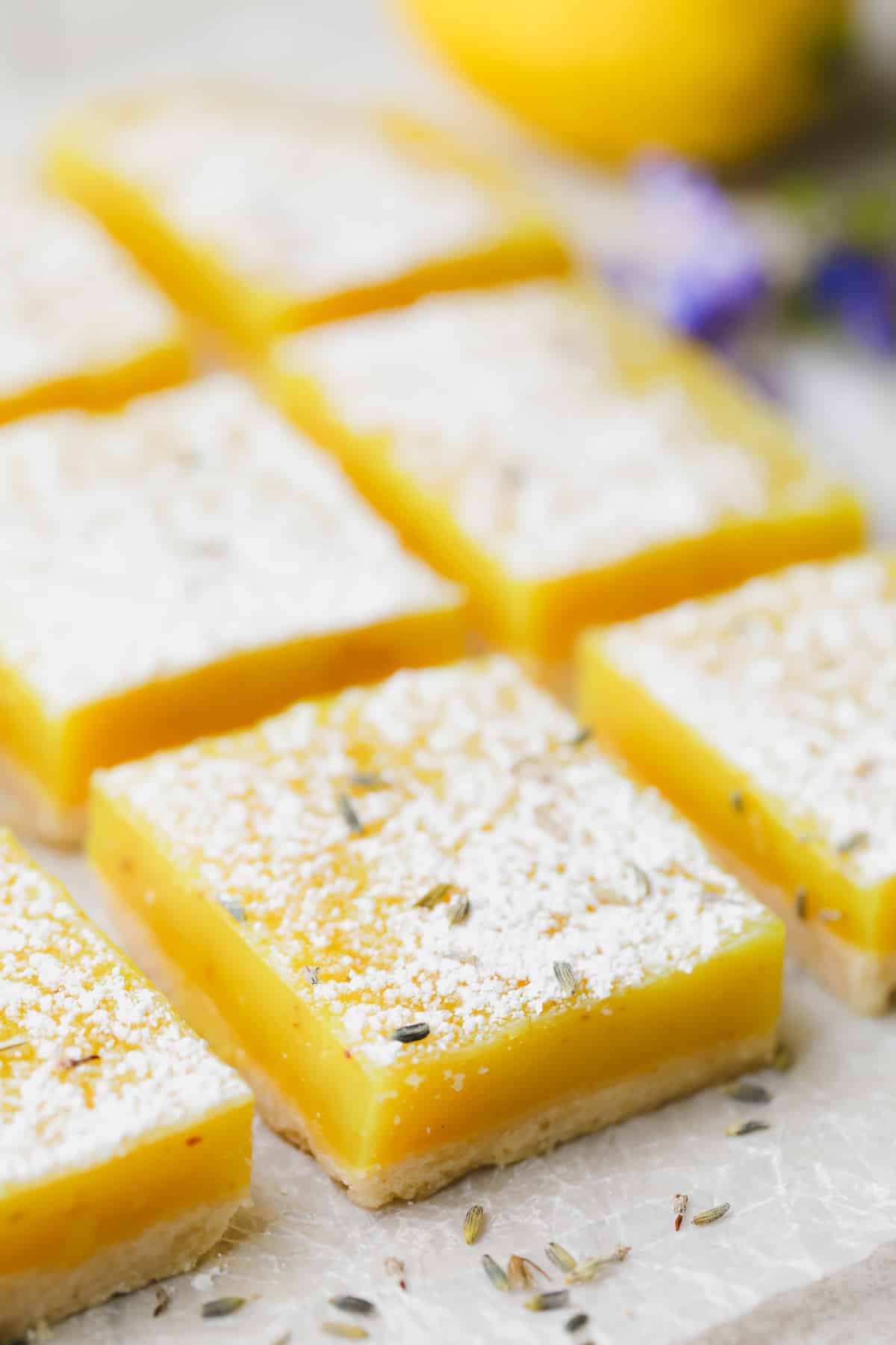 Side shot of several lemon squares with a lemon and purple flowers in the background