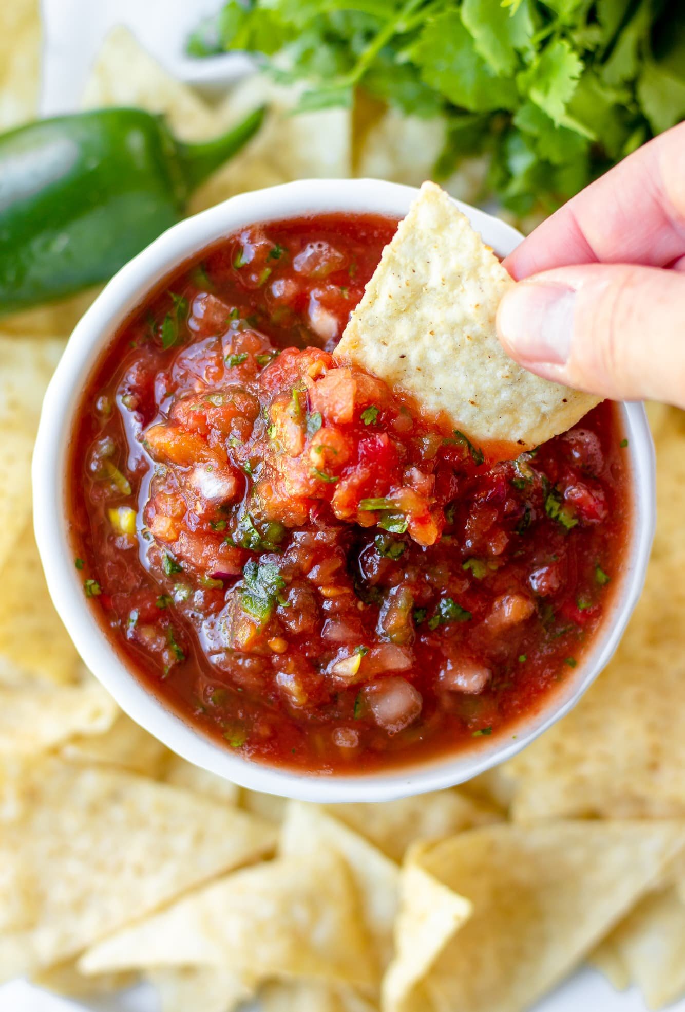 womans hand dipping a tortilla chip into a small bowl of tomato salsa.