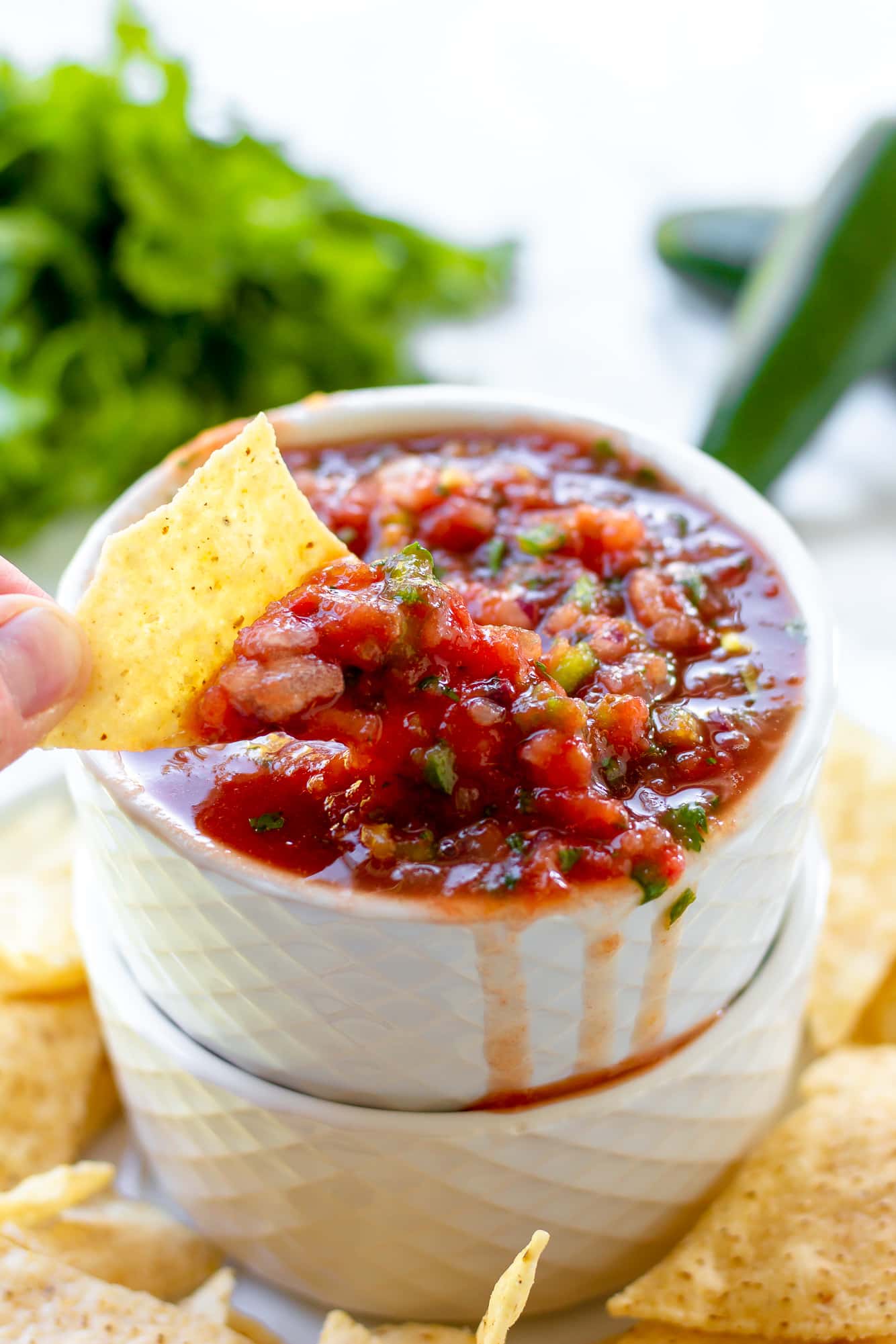 womans hand dipping a tortilla chip into a small bowl of tomato salsa.