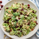 close up on vegan broccoli salad tossed in creamy dressing and topped with almonds in a large white bowl.