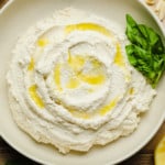 Vegan Ricotta cheese in a white bowl with olive oil drizzled on top and basil leaves on the side.