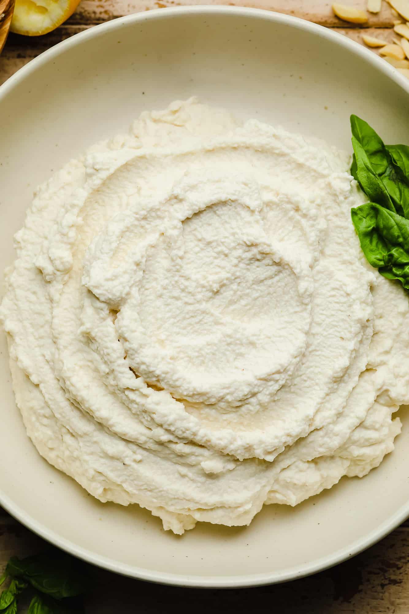 Vegan Ricotta cheese in a white bowl with basil leaves on the side.