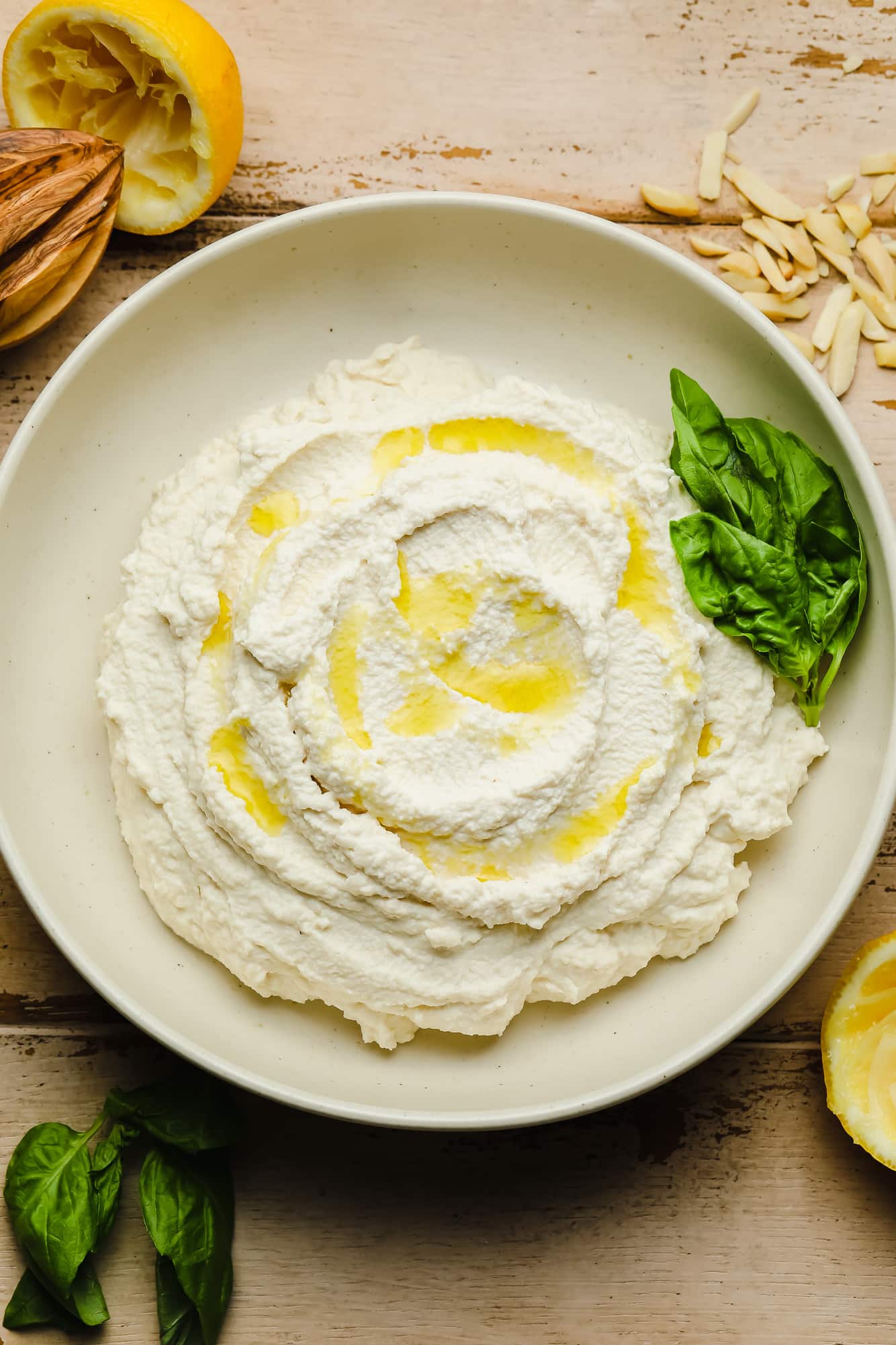 Vegan Ricotta cheese in a white bowl with olive oil drizzled on top and basil leaves on the side.