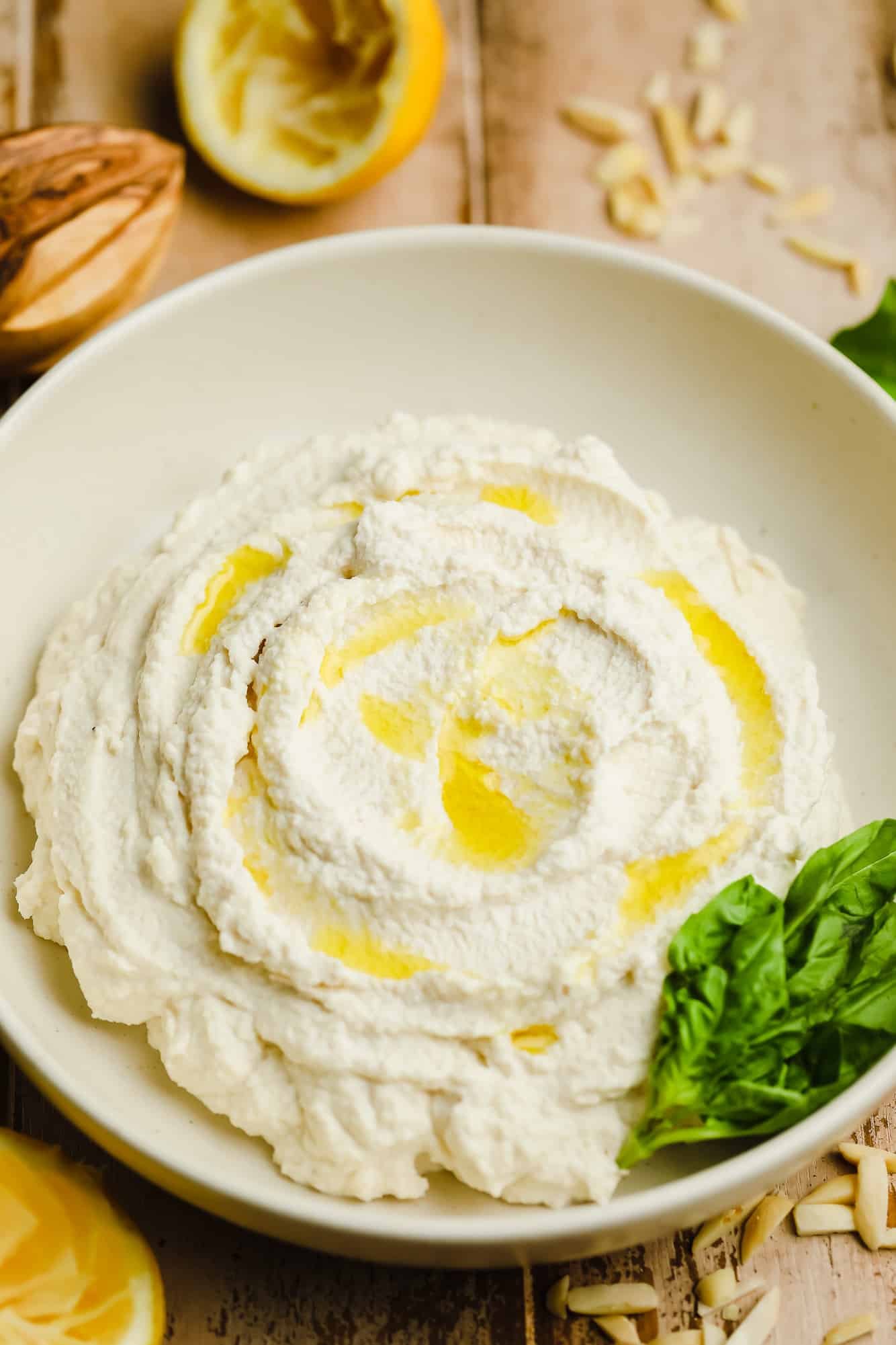 Vegan Ricotta cheese in a white bowl with olive oil drizzled on top and basil leaves on the side.