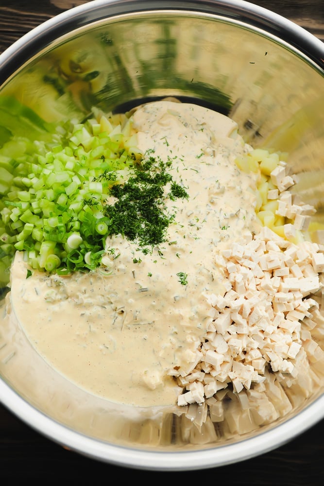 silver bowl on wood background with creamy sauce, celery, herbs and chopped tofu