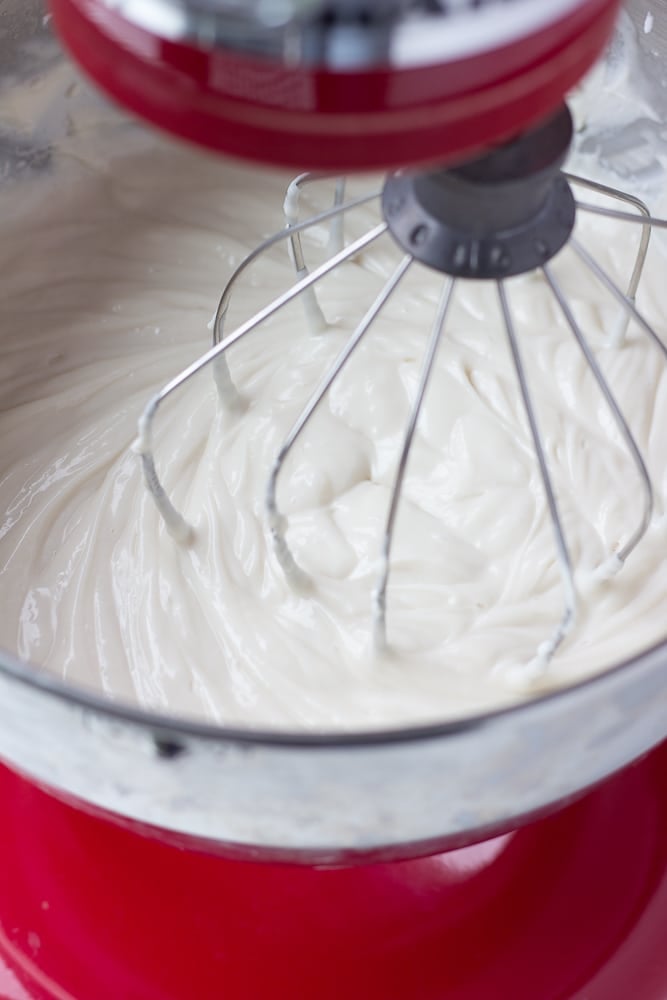 white cream in a red kitchen aid mixer with a whisk attachment
