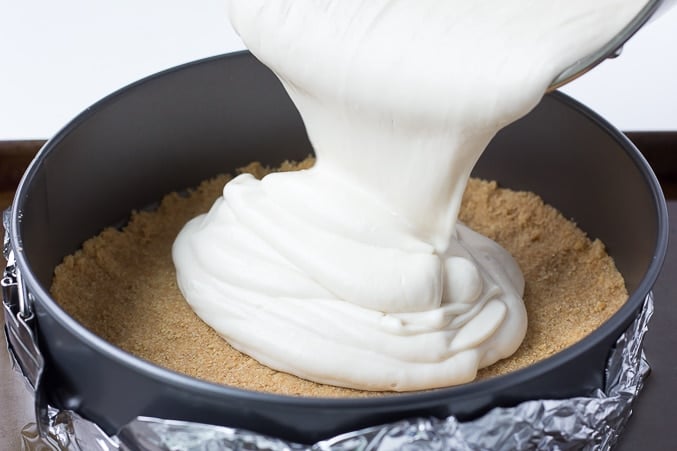 white vegan cheesecake filling being poured into the crust in a pan wrapped in foil