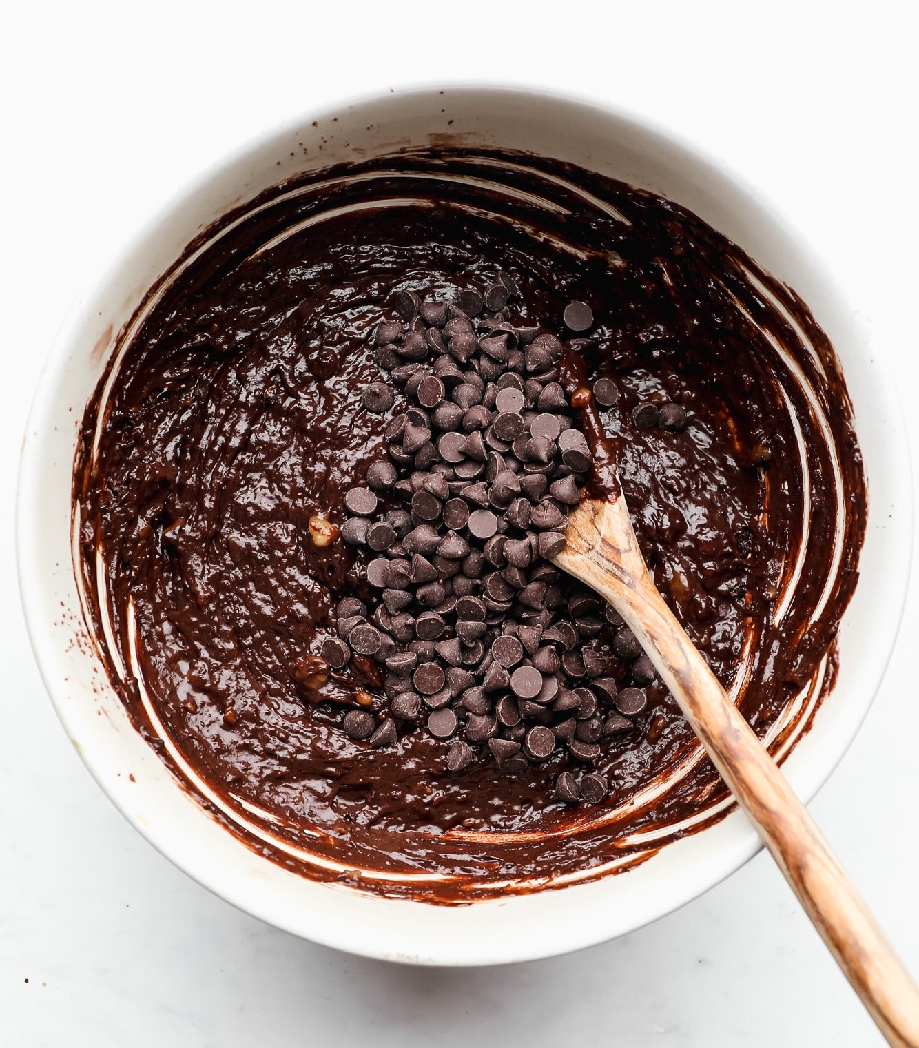 using a wooden spoon to stir chocolate chips into chocolate batter in a white bowl.