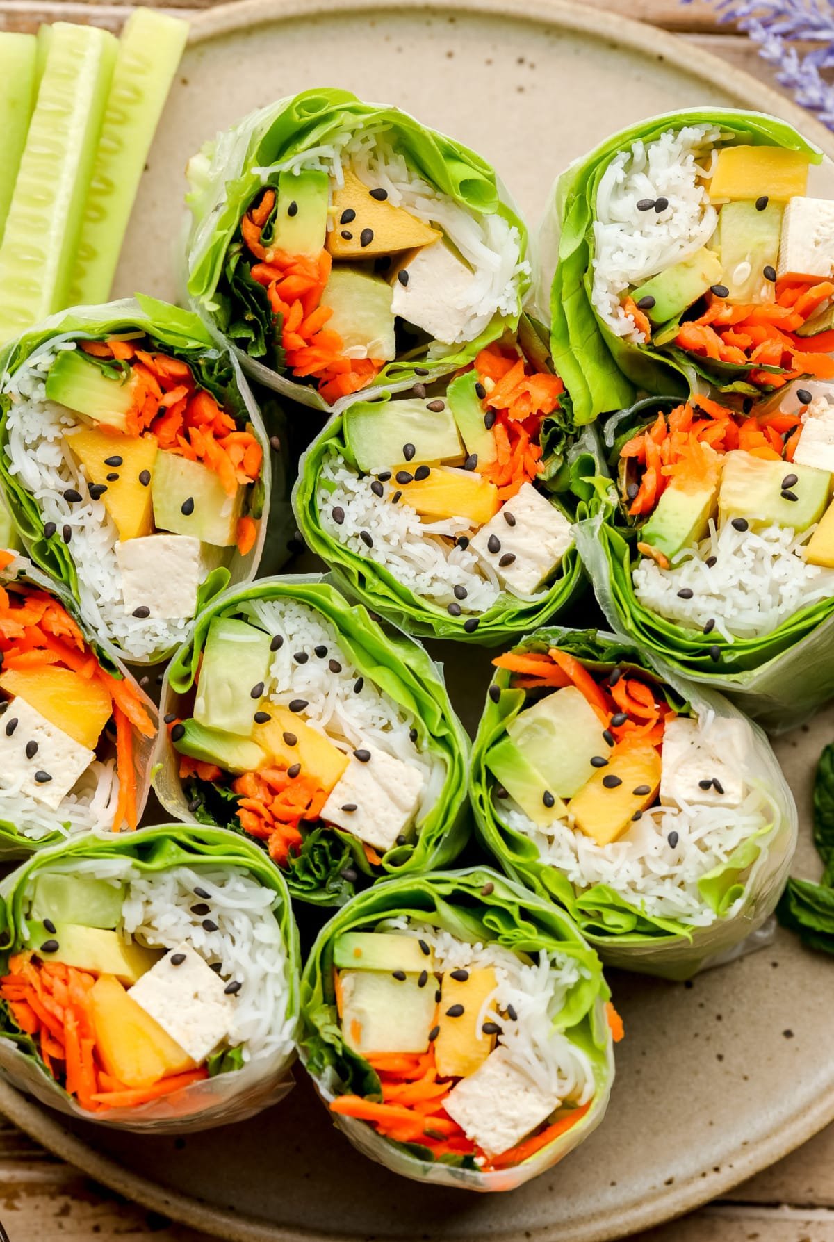 close up looking down on halved salad rolls with avocado, mango, noodles and lettuce.