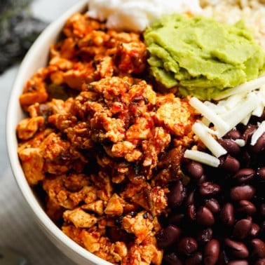 close up on a scoop of sofritas on a burrito bowl with black beans, shredded cheese, and guacamole.