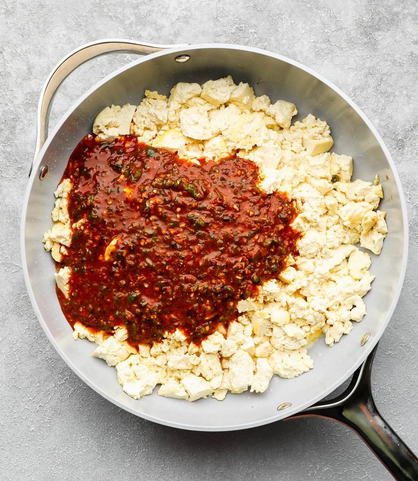 crumbled tofu in a large skillet with a red chili sauce poured on top.