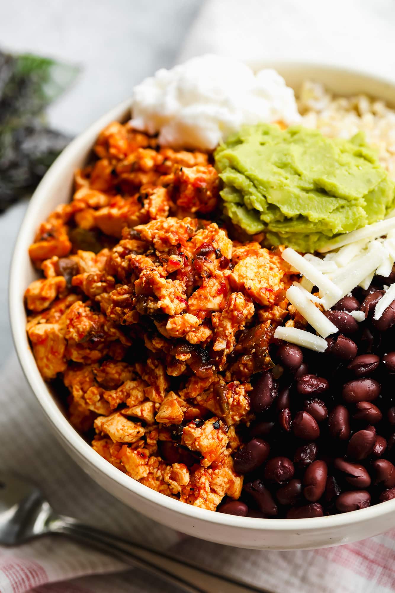 a vegan burrito bowl topped with sofritas, black beans, shredded cheese, and guacamole.