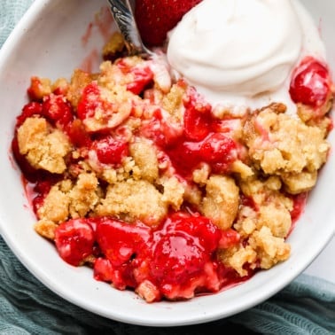 strawberry crumble in a white bowl with a scoop of vanilla ice cream.
