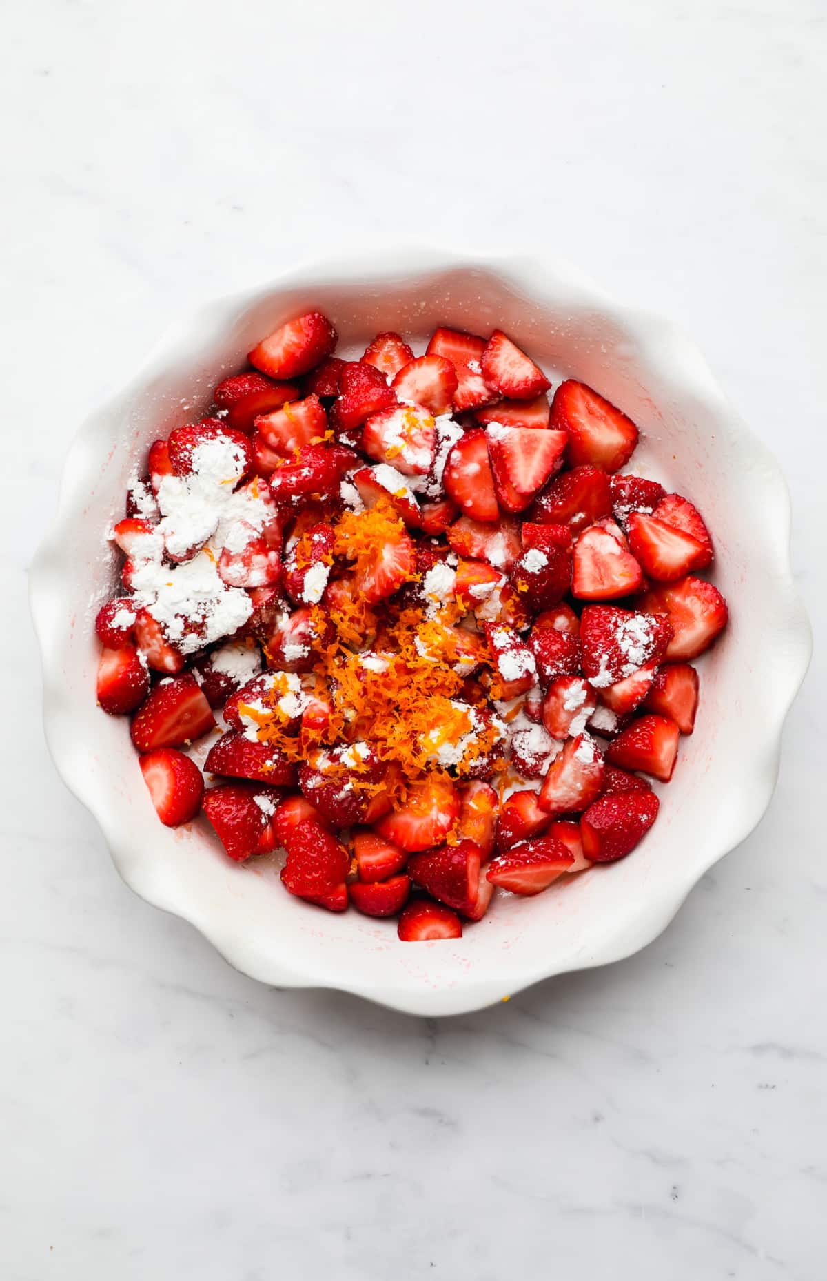 chopped strawberries topped with cornstarch and orange zest in a white pie dish.