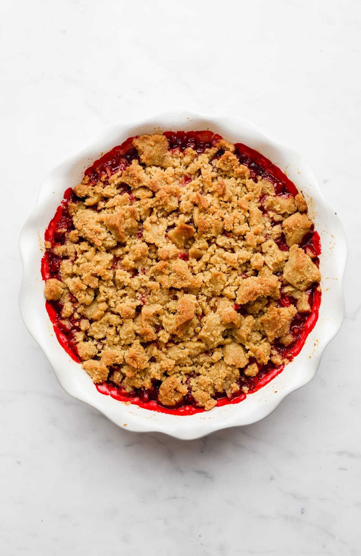 baked strawberry crumble in a white round dish.
