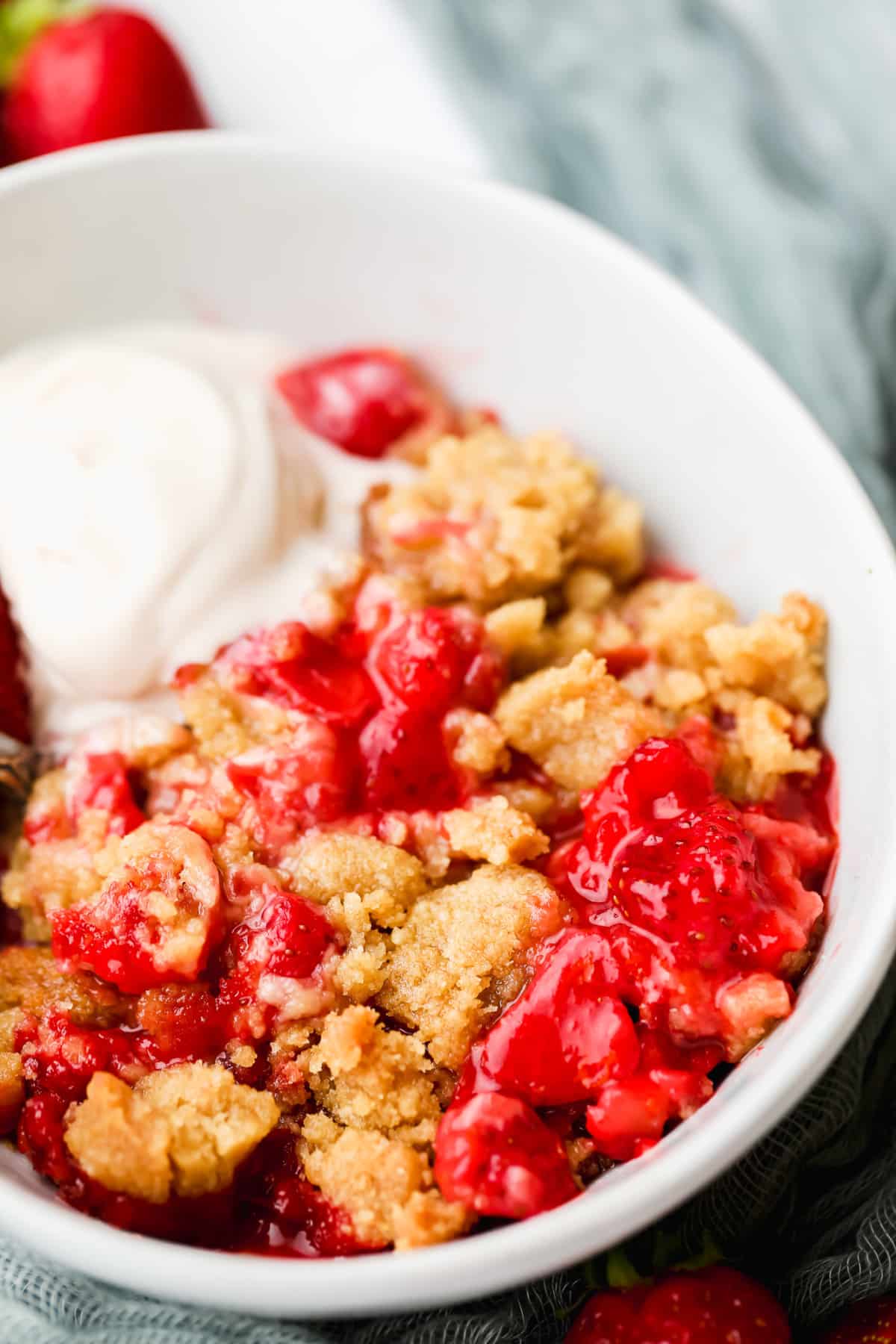 strawberry crumble in a white bowl with a scoop of vanilla ice cream.