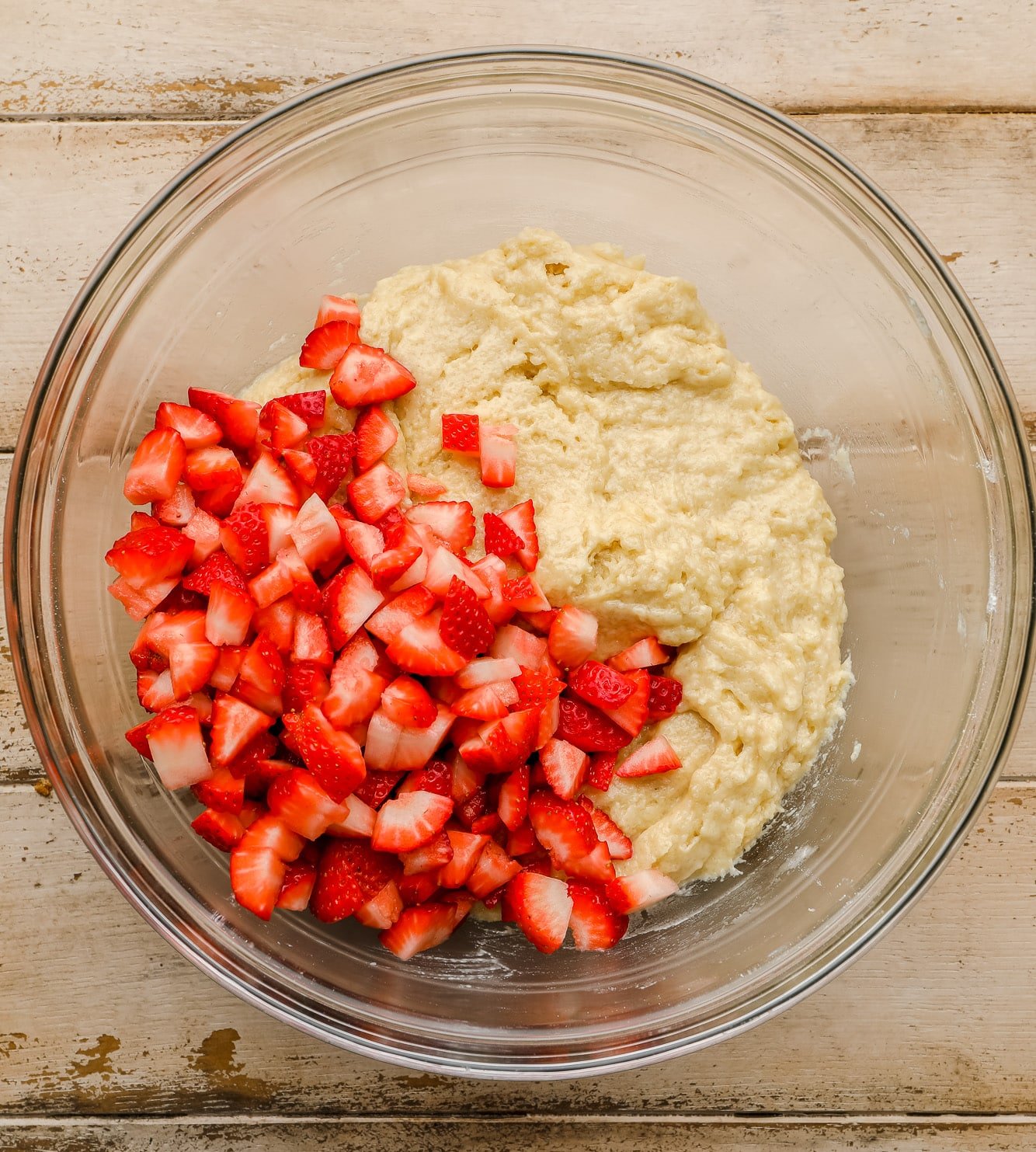 chopped strawberries on top of muffin batter in a large glass bowl.