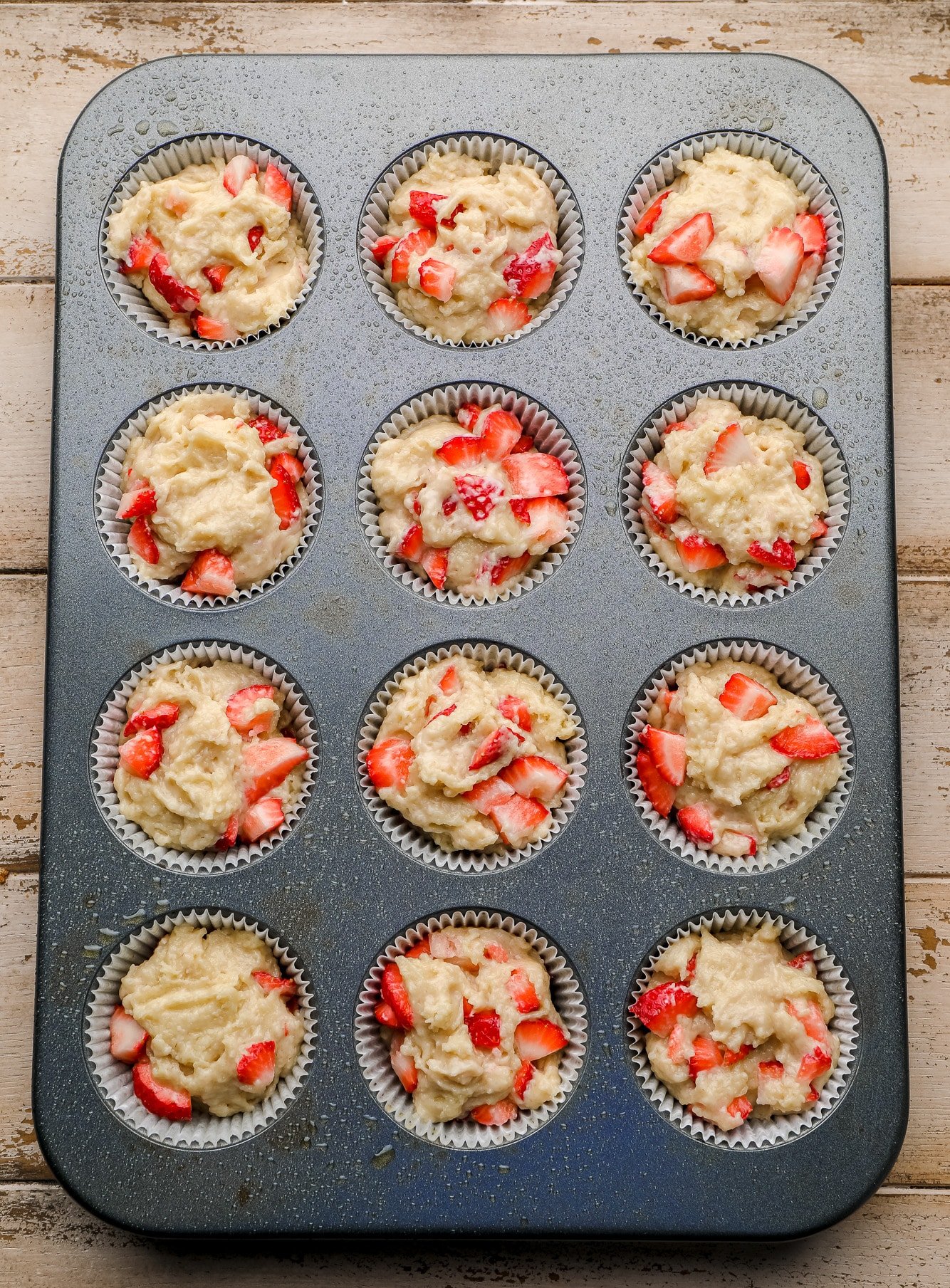 a muffin tin filled with strawberry muffin batter.