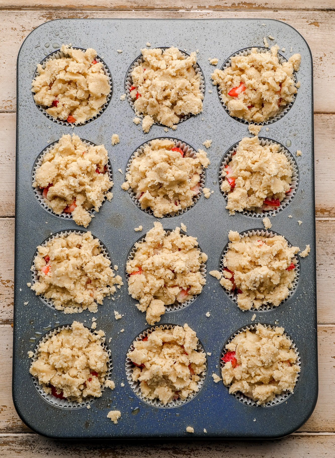 unbaked strawberry muffins in a muffin tin topped with a crumble.